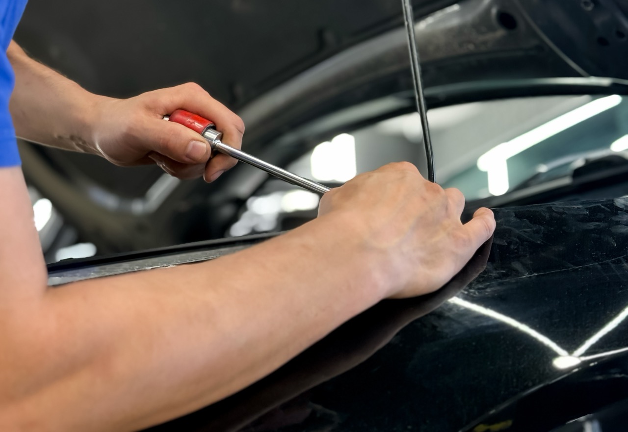 Process of paintless dent repair on car body. The mechanic at the auto shop with tools to repair dents in car body. Body repair. A specialist repairs a dent on the car body without painting. PDR.
