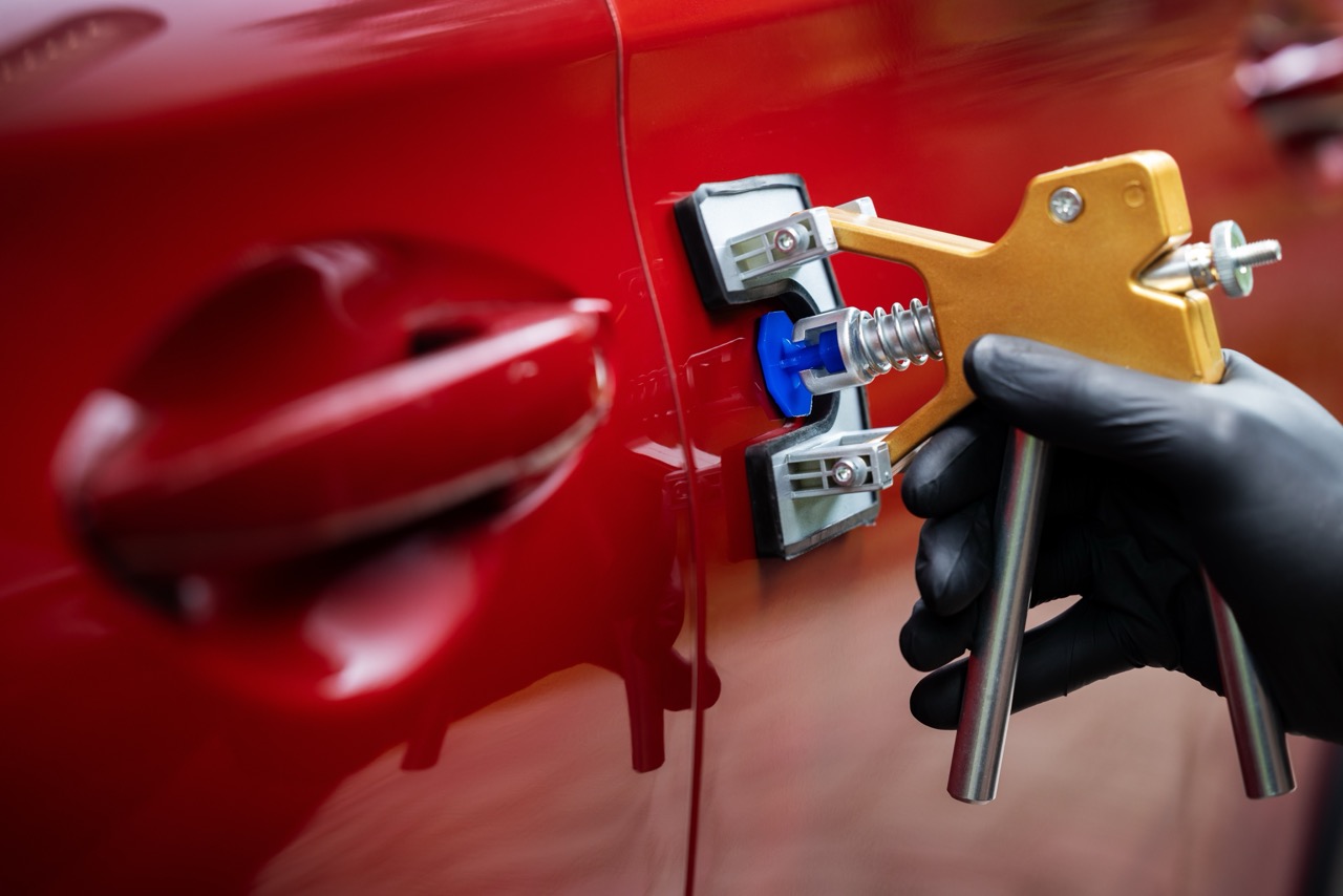 paintless car dent repair tool. man fixing red vehicle door with PDR technology